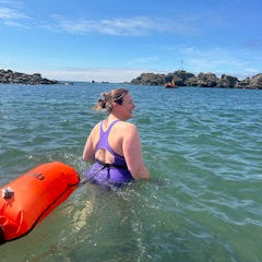 Woman in a purple swimsuit standing in the sea with a blue sky.